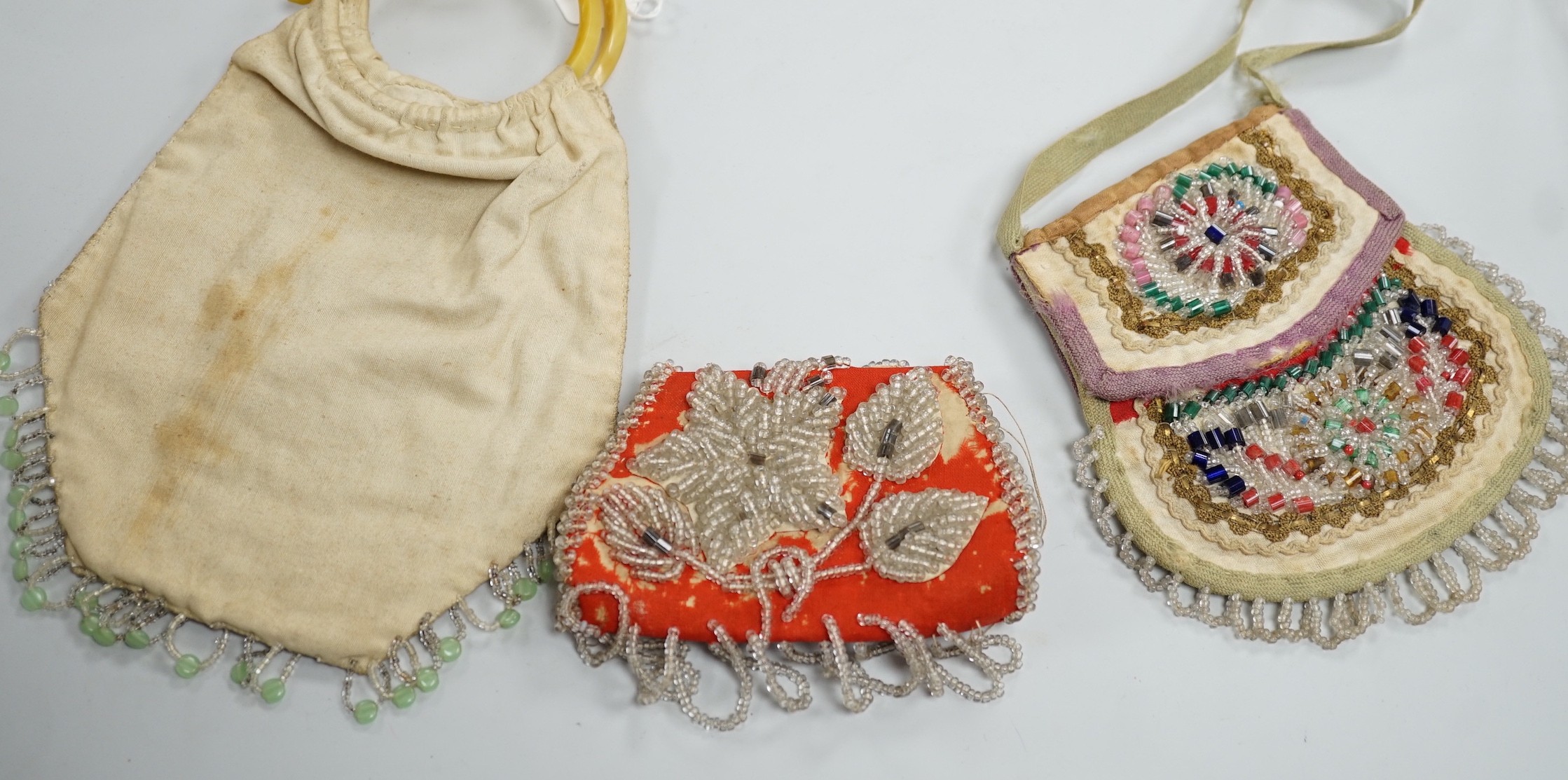 A mid to late 19th century Iroquois, North American/Canadian Indian glass beadwork bag on linen, together with a smaller red wool beaded purse and a 20th century suede embroidered bag with beaded fringe